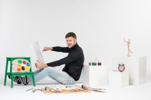 front-view-young-male-trying-draw-painting-with-tassel-white-wall-artist-paint-art-color-paint-picture-draw