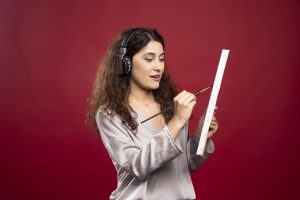 Woman in headphones painting on canvas over red background. High quality photo